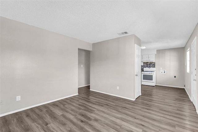 unfurnished living room featuring a textured ceiling, wood finished floors, visible vents, and baseboards