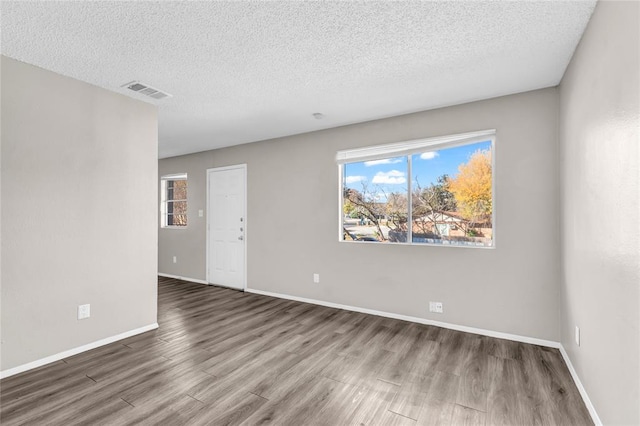 unfurnished room featuring visible vents, a textured ceiling, baseboards, and wood finished floors