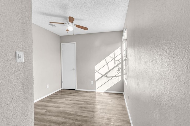 spare room featuring baseboards, visible vents, a ceiling fan, wood finished floors, and a textured ceiling