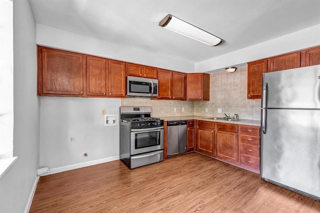 kitchen featuring stainless steel appliances, a sink, light countertops, light wood-type flooring, and backsplash