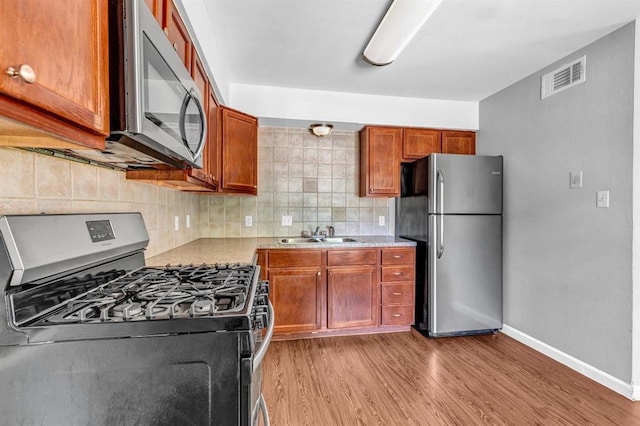 kitchen with visible vents, light wood-style flooring, a sink, stainless steel appliances, and backsplash