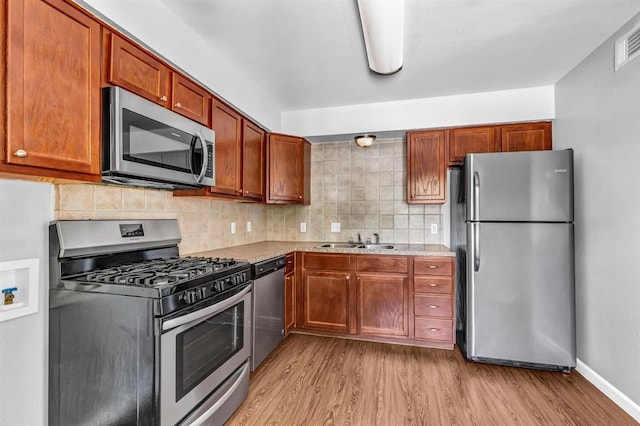 kitchen featuring stainless steel appliances, a sink, baseboards, light wood-style floors, and backsplash