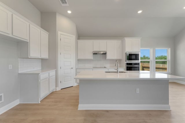 9908 Ephemeral Dr, Manor, TX 78653 - kitchen featuring stainless steel oven, built in microwave, under cabinet range hood, an island with sink, and tasteful backsplash