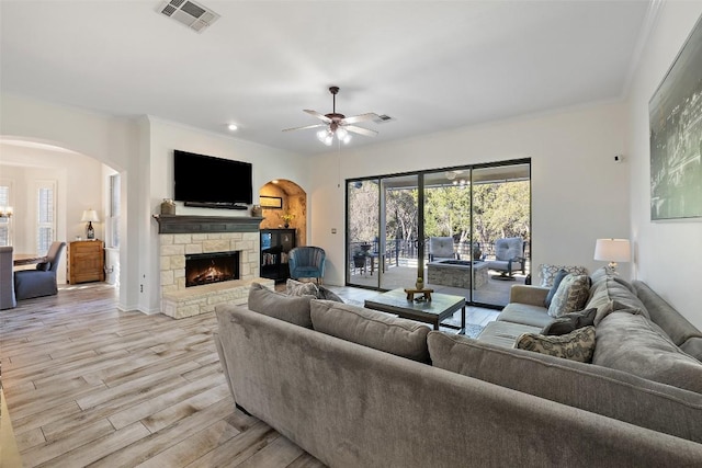22128 Rose Grass Ln, Spicewood, TX 78669 - living room with arched walkways, light wood-type flooring, a stone fireplace, ceiling fan, and crown molding