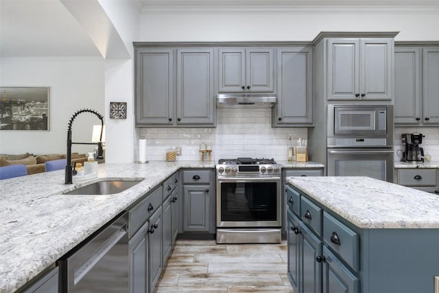 kitchen with under cabinet range hood, gray cabinetry, a sink, ornamental molding, and appliances with stainless steel finishes