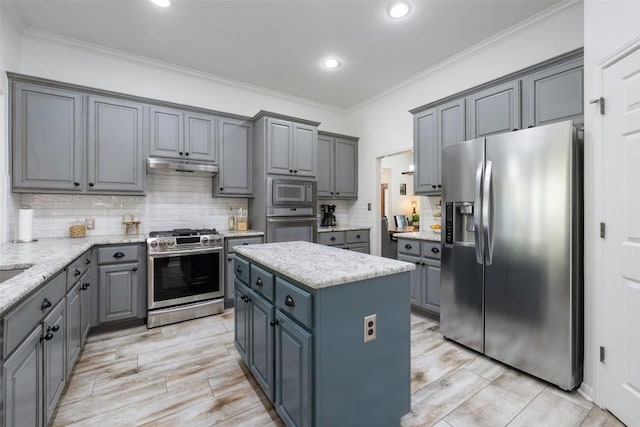 kitchen with gray cabinets, appliances with stainless steel finishes, ornamental molding, a kitchen island, and under cabinet range hood