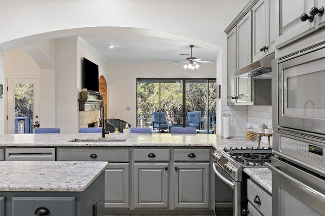 kitchen featuring under cabinet range hood, a peninsula, backsplash, gray cabinets, and gas stove