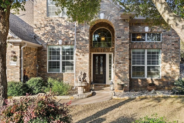 doorway to property with a shingled roof and brick siding