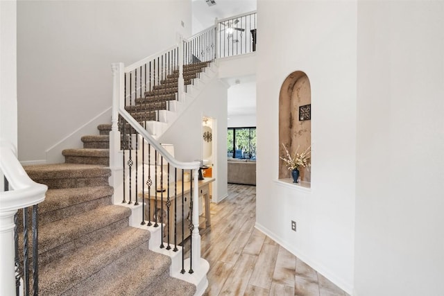 staircase with a towering ceiling, baseboards, and wood finished floors