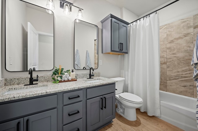 full bathroom featuring toilet, double vanity, a sink, and wood finished floors