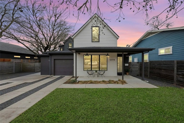 view of front facade with a yard, covered porch, driveway, and fence