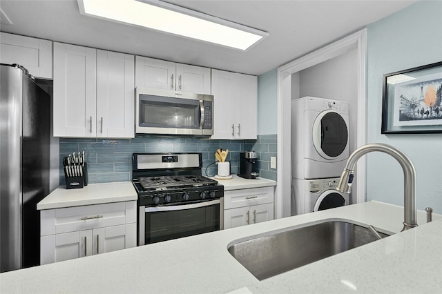 kitchen featuring tasteful backsplash, appliances with stainless steel finishes, stacked washing maching and dryer, white cabinetry, and a sink