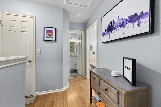 hall with light wood finished floors, attic access, and baseboards