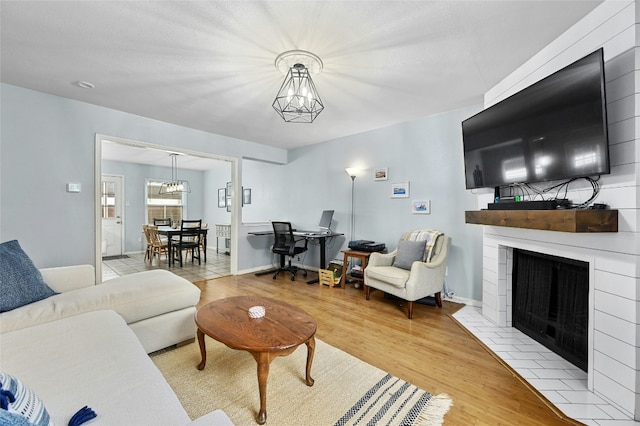 living area featuring a chandelier, a fireplace with flush hearth, baseboards, and wood finished floors