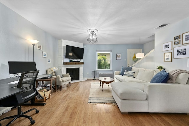 living room with visible vents, a brick fireplace, wood finished floors, and a chandelier