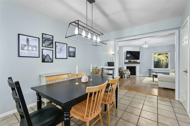 dining area with baseboards, a brick fireplace, and light tile patterned flooring