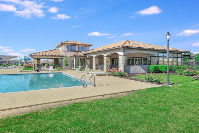 rear view of house featuring a patio, stone siding, a tiled roof, a community pool, and a yard