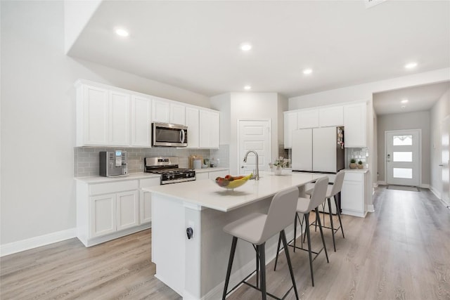 kitchen featuring a breakfast bar, stainless steel appliances, white cabinets, an island with sink, and light wood-type flooring