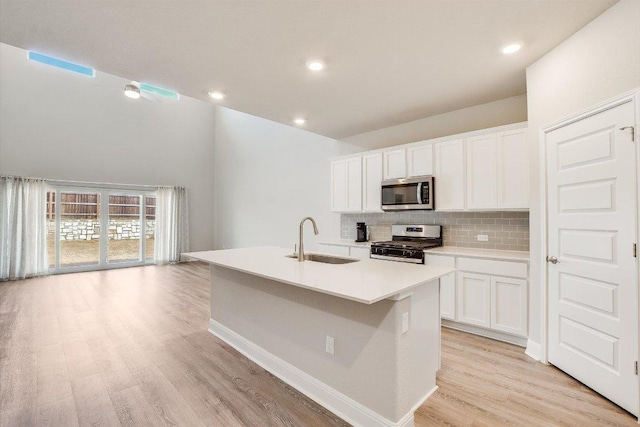 kitchen with a kitchen island with sink, a sink, light wood-style floors, appliances with stainless steel finishes, and tasteful backsplash