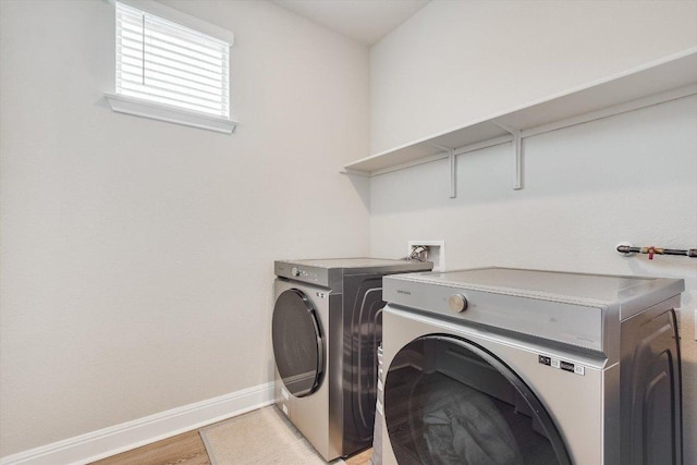 clothes washing area featuring laundry area, washing machine and dryer, light wood-style flooring, and baseboards