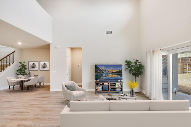 living area with stairs, a high ceiling, wood finished floors, and visible vents