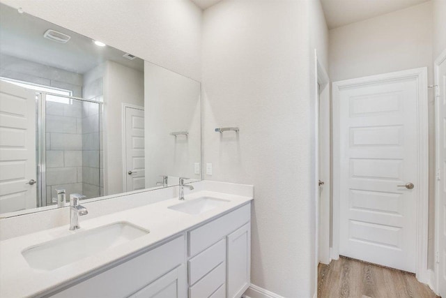 full bathroom with a stall shower, double vanity, a sink, and wood finished floors