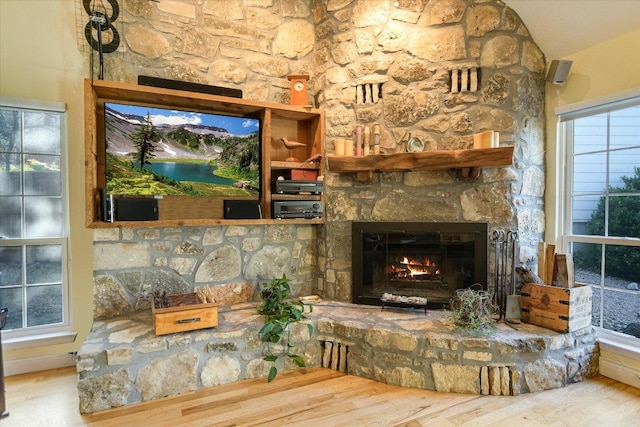 living room with lofted ceiling, a stone fireplace, and wood finished floors