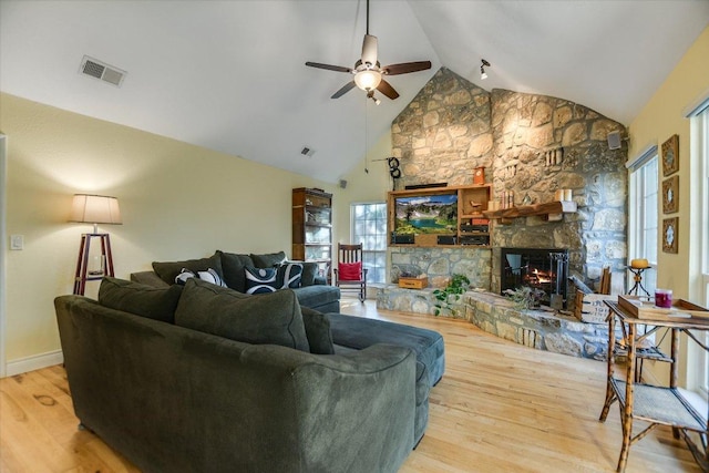 living room featuring baseboards, visible vents, wood finished floors, a stone fireplace, and high vaulted ceiling