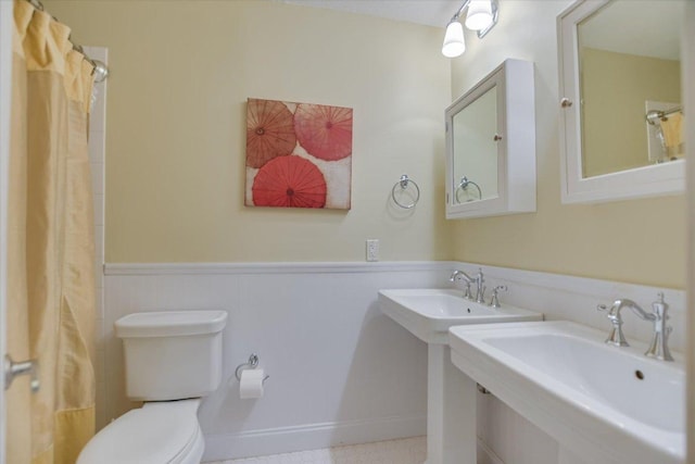 bathroom with a shower with shower curtain, a wainscoted wall, a sink, and toilet