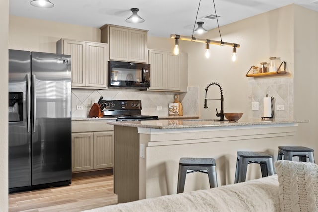 kitchen with decorative backsplash, a peninsula, light stone countertops, black appliances, and a kitchen bar