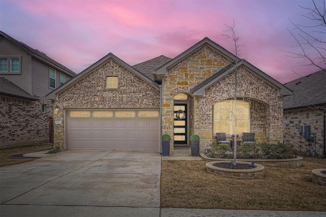 french country inspired facade with a garage, concrete driveway, brick siding, and stone siding