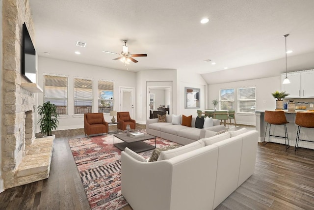 living area featuring dark wood-style floors, recessed lighting, visible vents, ceiling fan, and a stone fireplace