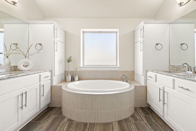 full bathroom featuring a garden tub, wood finish floors, two vanities, and a sink