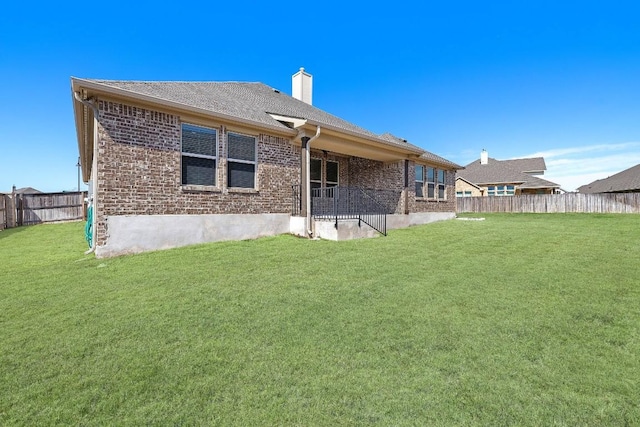 back of house with a yard, brick siding, a chimney, and fence