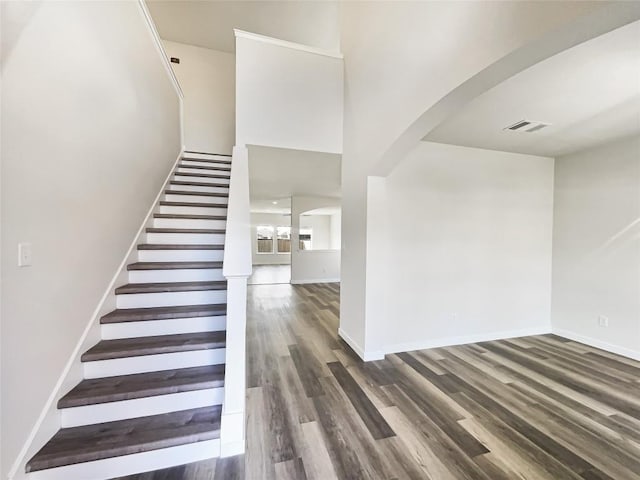 stairway with baseboards, arched walkways, and wood finished floors