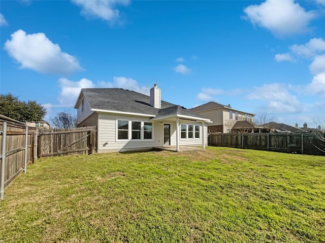 back of house with a fenced backyard, a yard, and a chimney