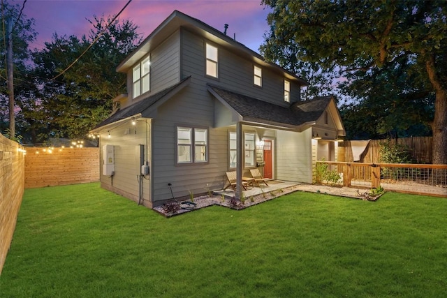 back of house at dusk with a lawn, a patio area, and a fenced backyard