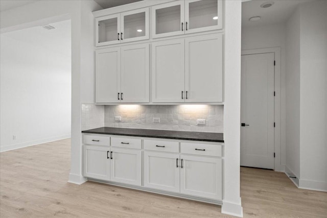 kitchen featuring dark countertops, light wood finished floors, tasteful backsplash, and white cabinetry