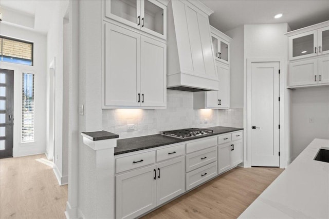 kitchen with light wood-style floors, custom range hood, stainless steel gas stovetop, and tasteful backsplash