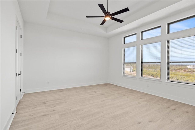 unfurnished room featuring ceiling fan, a raised ceiling, light wood-style flooring, and baseboards