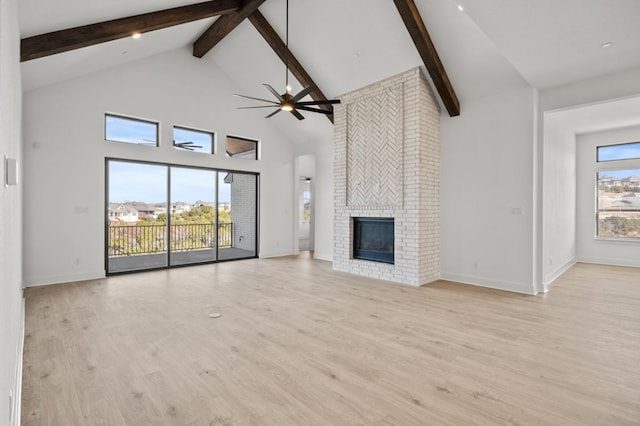 unfurnished living room with ceiling fan, beamed ceiling, a brick fireplace, and light wood-style floors