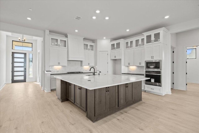 kitchen with light wood-style flooring, white cabinets, stainless steel oven, a sink, and built in microwave