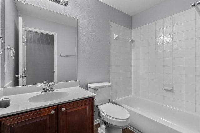 full bath featuring toilet, a textured wall, washtub / shower combination, and vanity