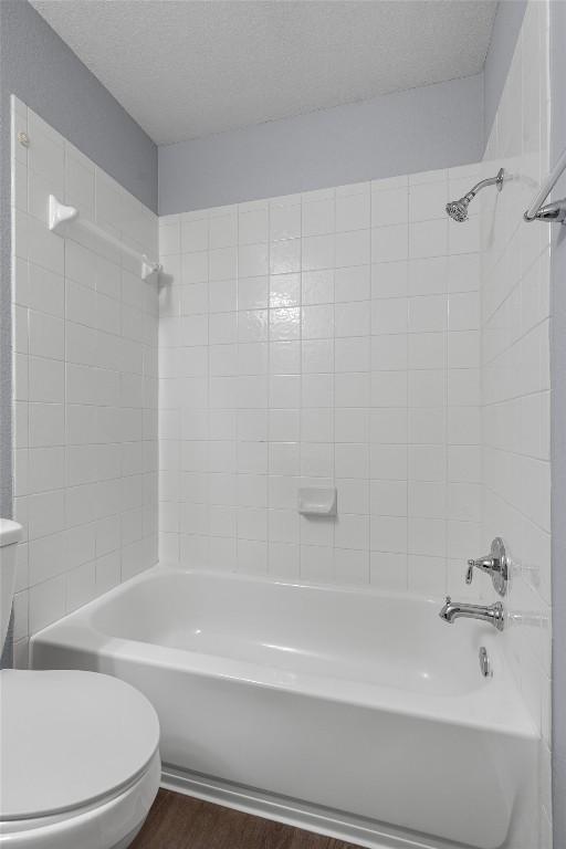 bathroom with toilet,  shower combination, a textured ceiling, and wood finished floors