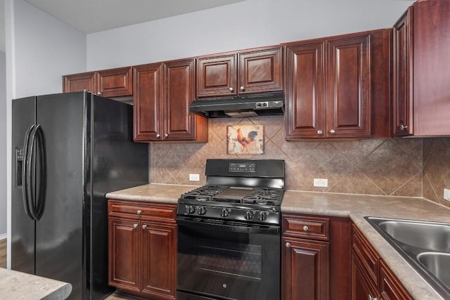 kitchen with under cabinet range hood, a sink, light countertops, black appliances, and tasteful backsplash