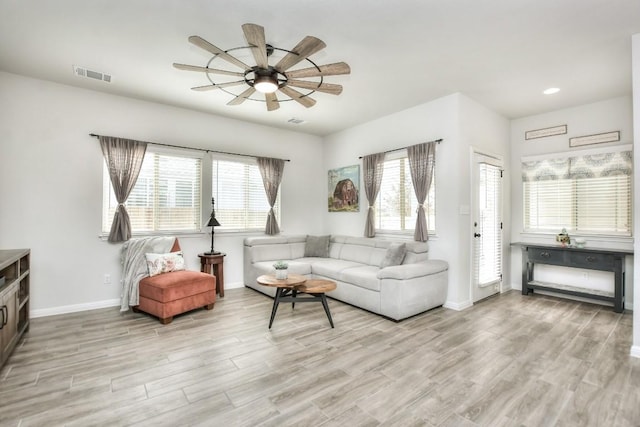 living room featuring light wood finished floors, a ceiling fan, visible vents, and baseboards