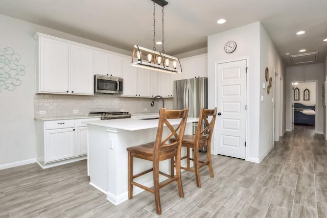 kitchen featuring a center island with sink, decorative backsplash, appliances with stainless steel finishes, light countertops, and a sink