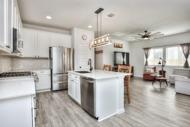 kitchen featuring a sink, visible vents, open floor plan, appliances with stainless steel finishes, and decorative backsplash