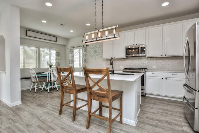 kitchen with stainless steel appliances, white cabinetry, light countertops, decorative backsplash, and an island with sink