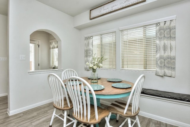 dining area with arched walkways, wood finished floors, a wealth of natural light, and baseboards